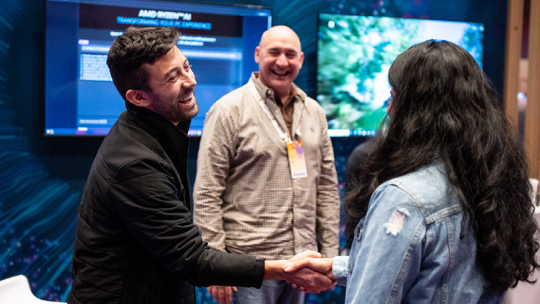 Image 1: Two people shaking hands in the foreground with a third person observing from the background and laughing